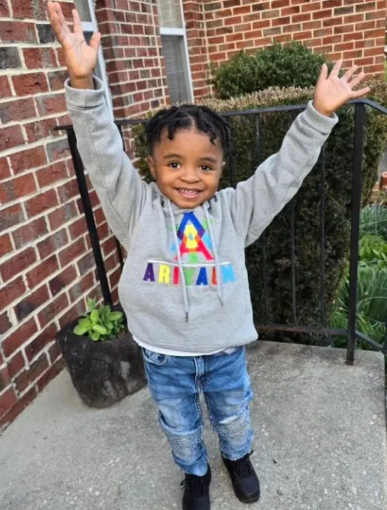 Child in a grey Ariyaun hoodie with arms raised